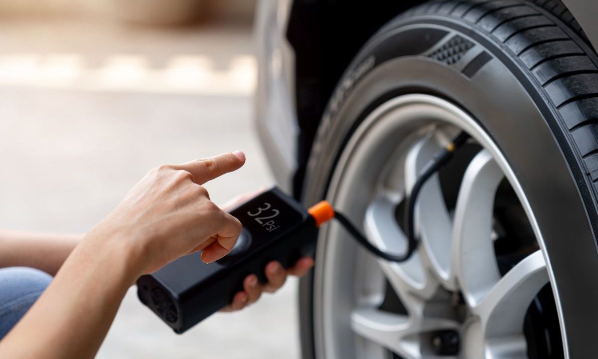 Hand holding a cordless tire inflator on a car tire valve