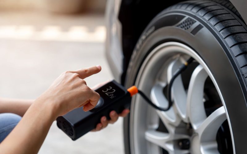 Hand holding a cordless tire inflator on a car tire valve