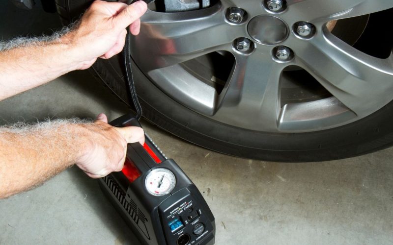 Portable air compressor topping off a car tire at the wheel